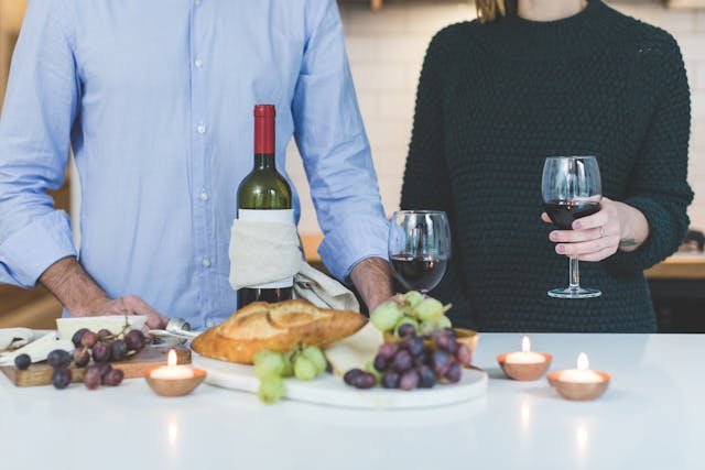 man-standing-beside-woman-holding-wine-glass-in-front-of-grapes-and-bread-on-table